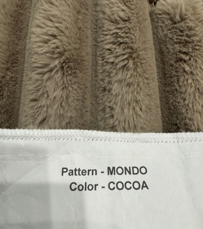 Close-up of a textured fabric with 'Pattern - MONDO' and 'Color - COCOA' text on a white label.