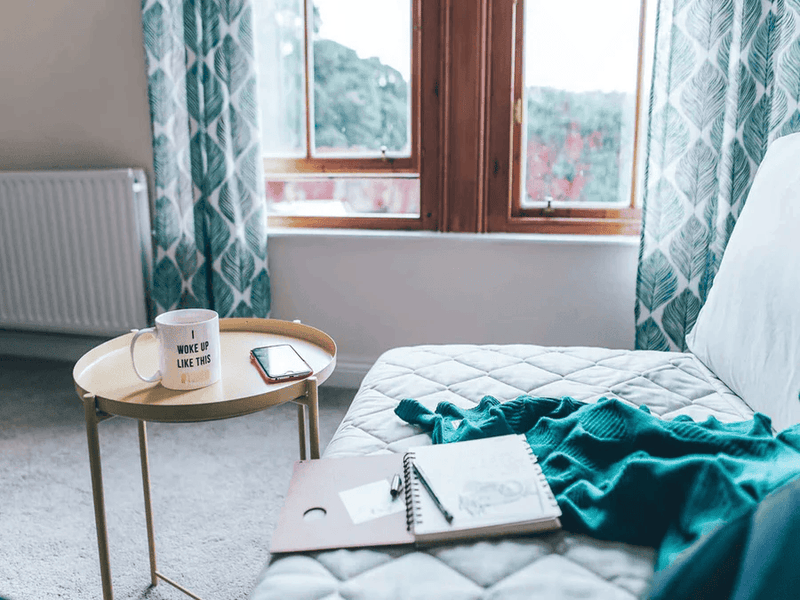 Gray daybed with green fabric, small round table and a notebook on top of it